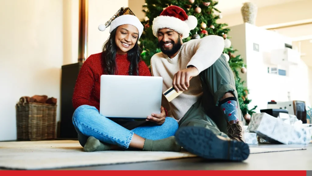 Couple with Christmas hats holding a laptop and buying gifts online